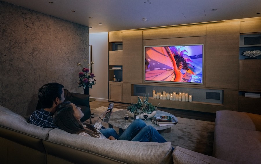 A couple on a couch watches TV in a dimly lit room.